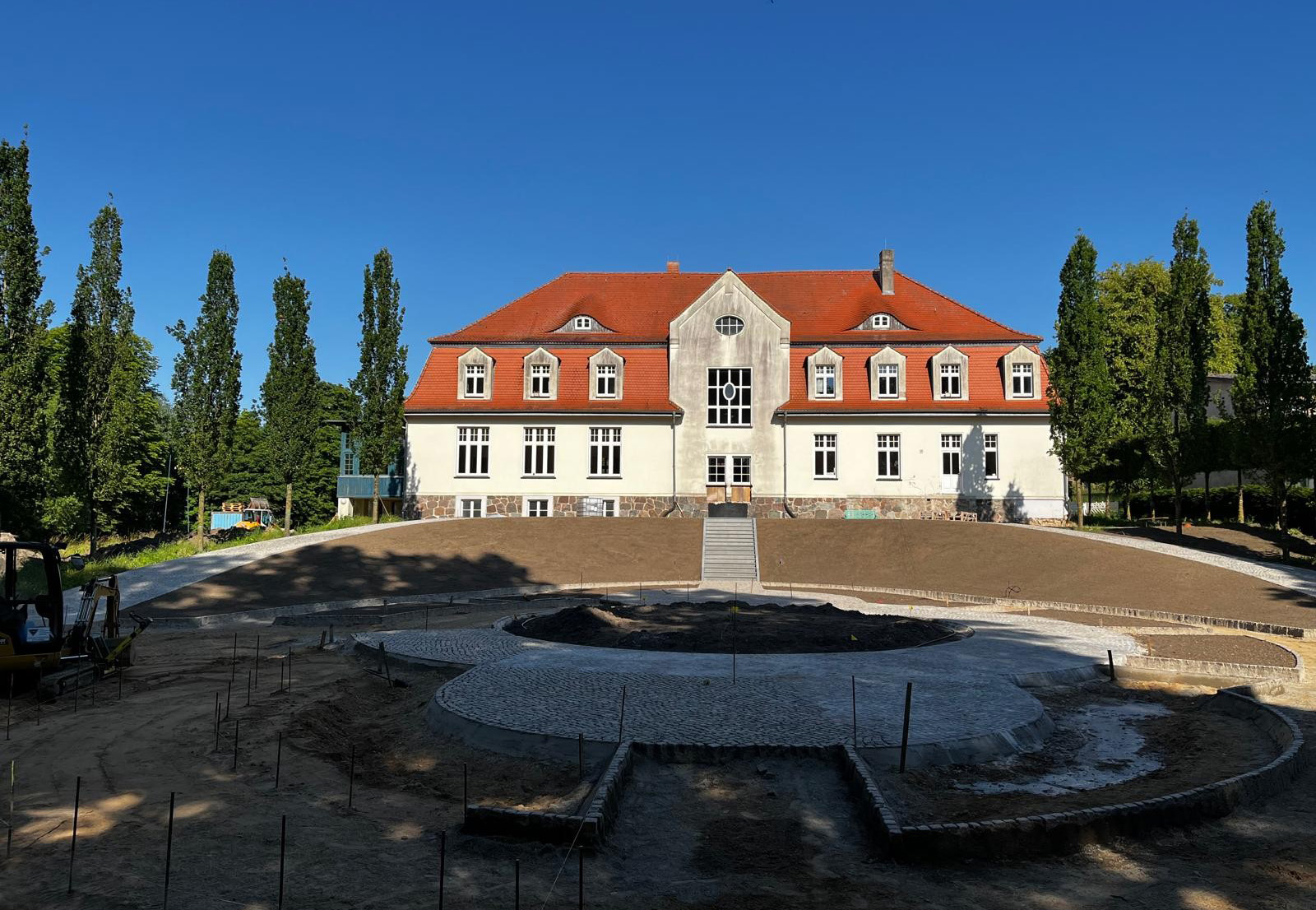 Sommertag der Blick auf ein großes Gutshaus mit tollen neuen Bäumen rechts und links.